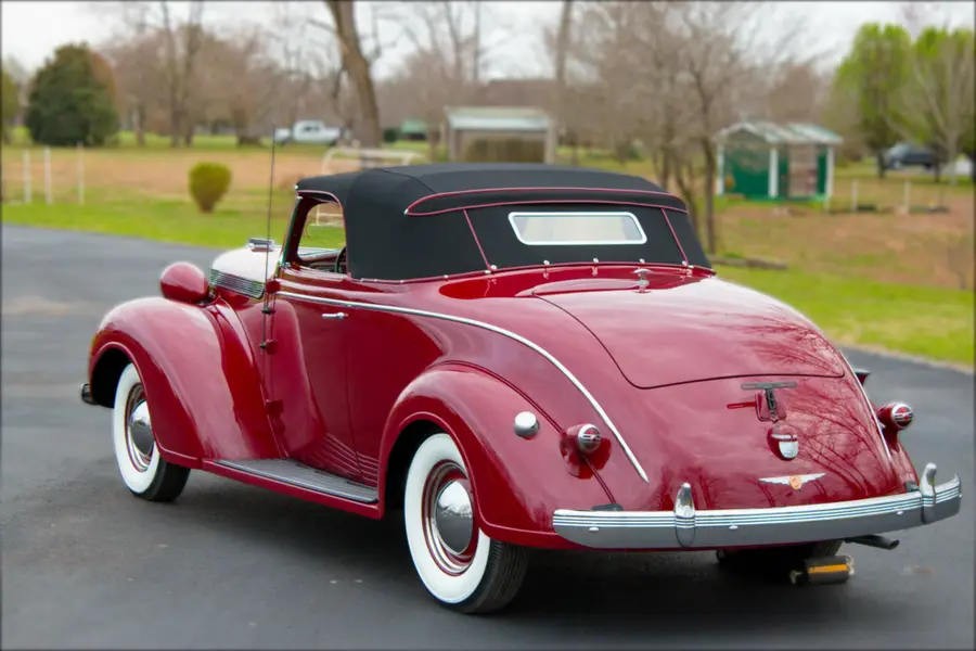 A restored red convertible roadster, rear three-quarter.