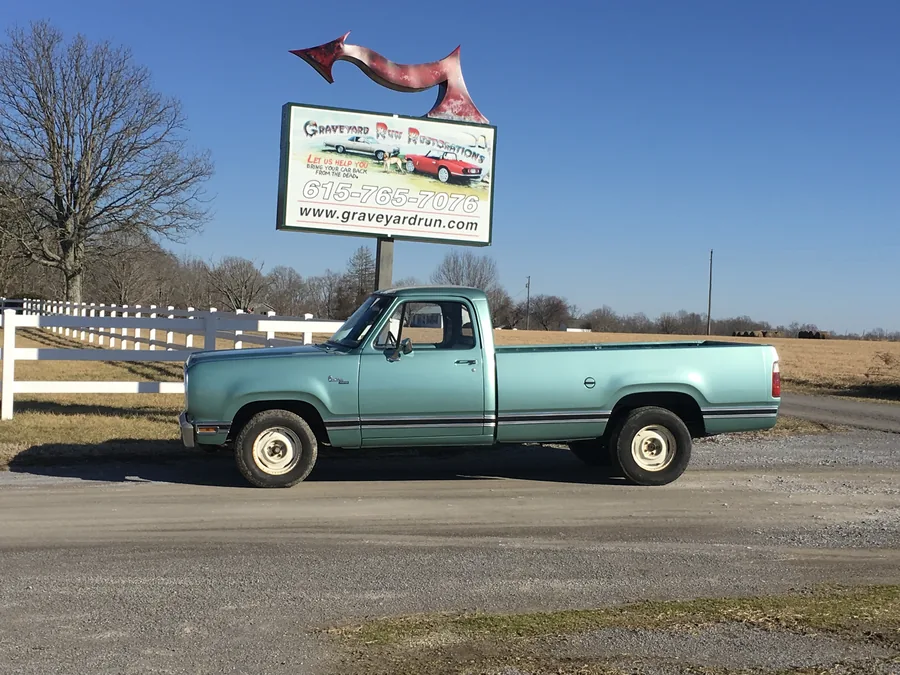 The 1979 Dodge pickup in seafoam green beside the Graveyard Run roadside sign.