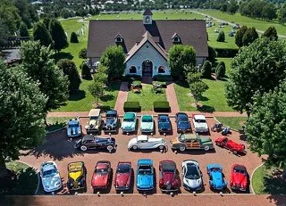 Aerial view of the Keeneland Concours d’Elegance winner circle: two rows of classic cars parked on a brick circle in front of a white building.