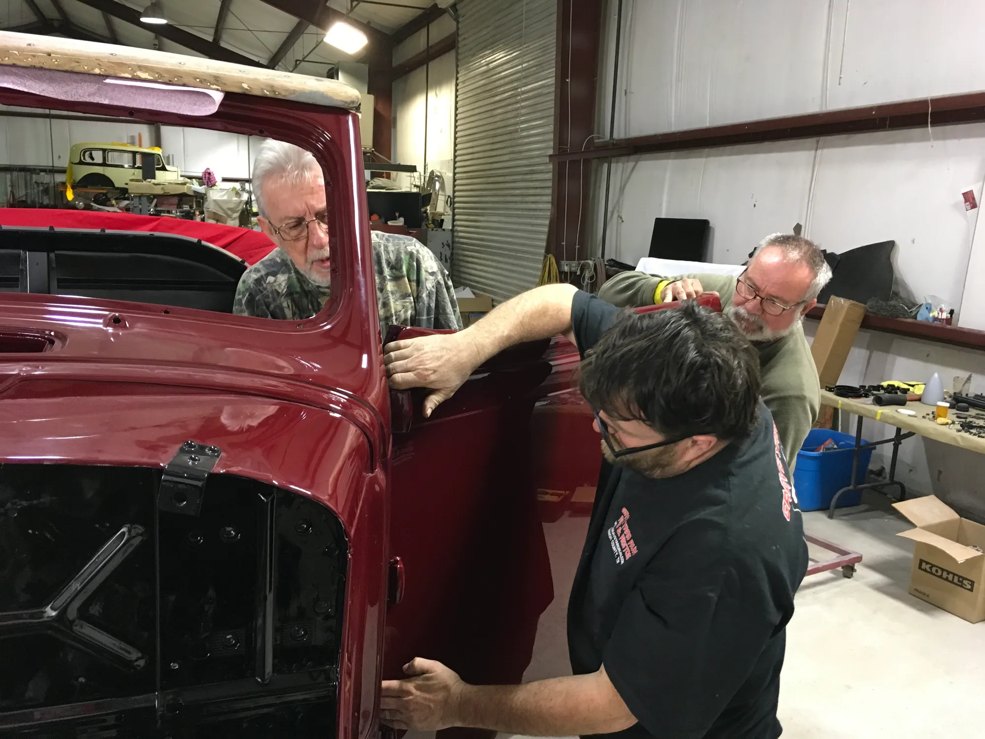 Three men fitting and adjusting the door on a red classic body in the shop.