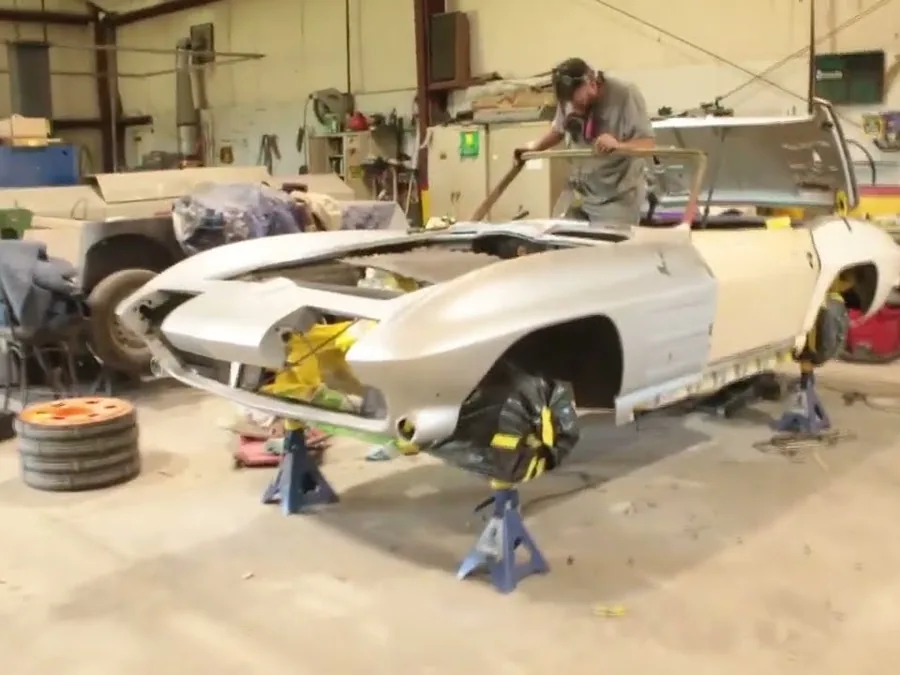 The 1964 Corvette Stingray stripped to its body on jack stands in the shop, front clip off.
