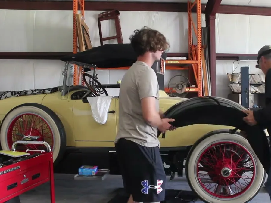 The yellow 1921 Haynes Special Roadster with red wire wheels, fenders coming off for teardown in the shop.