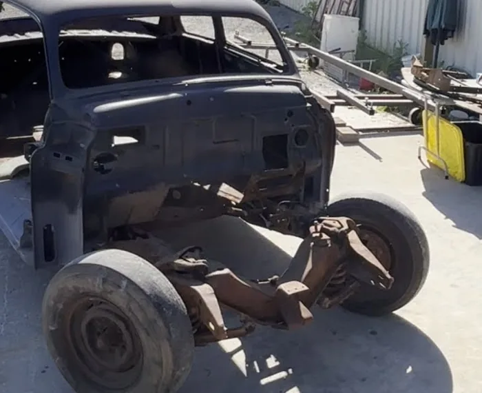 The 1951 Mercury coupe stripped to a bare body shell on its chassis outside the shop.